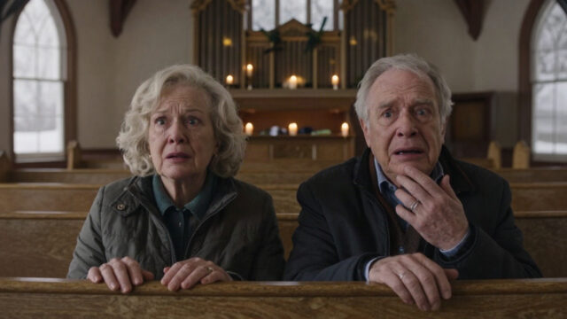 A snowy Christmas Eve at a small Catholic church in Milwaukee, seen from the organ loft. Warm candlelight glows over rows of wooden pews, with two older figures seated together at